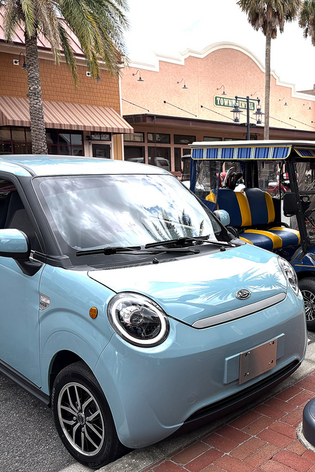 Small blue car parked on a street with palm trees and buildings in the background